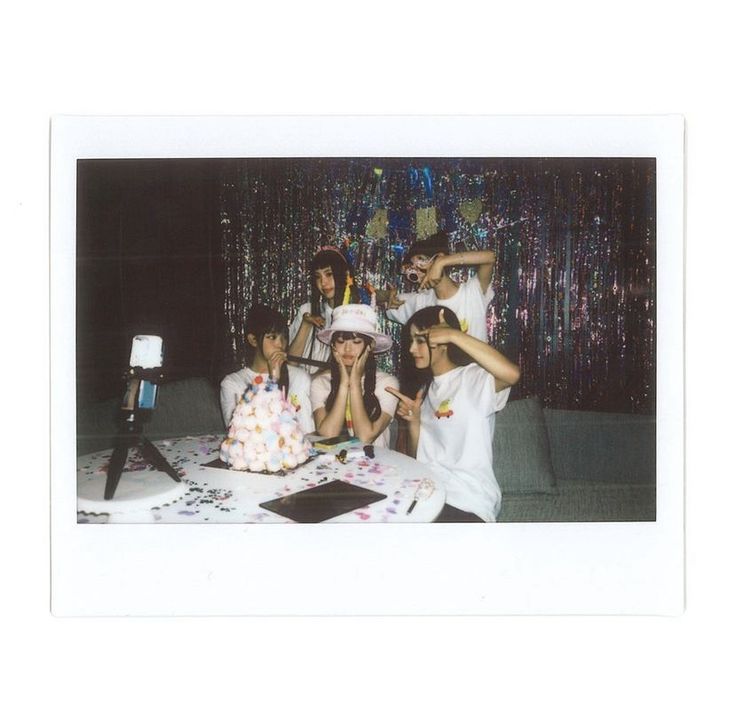 a group of people sitting at a table with a cake in front of them and a camera