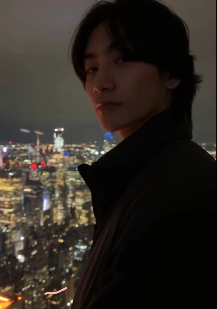 a man standing in front of a cityscape at night with the lights on