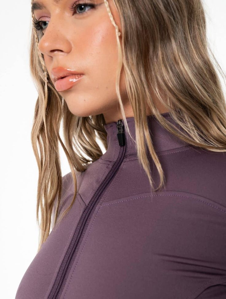 a woman with long hair wearing a purple wetsuit and ear piercings, looking off to the side