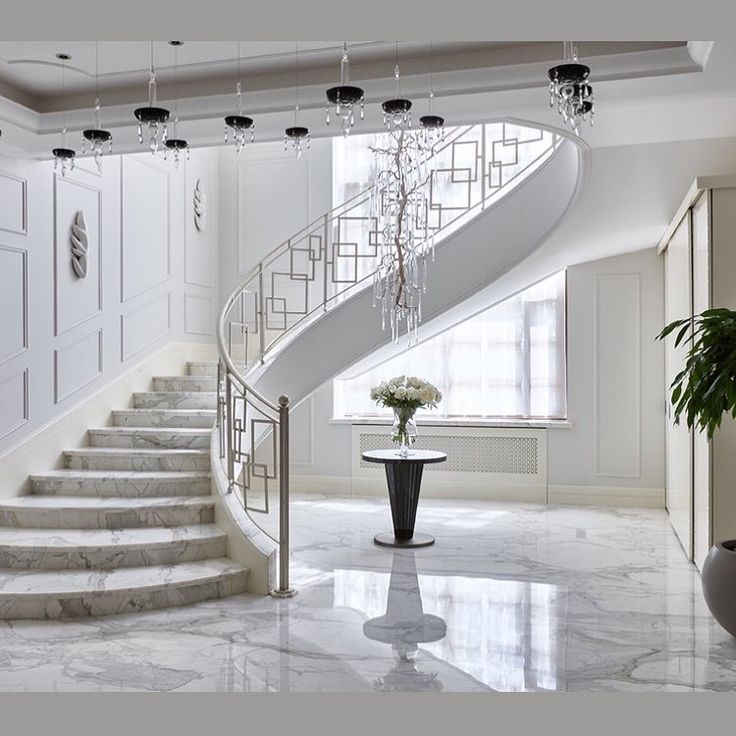 a white staircase with chandelier and potted plant next to it on the floor