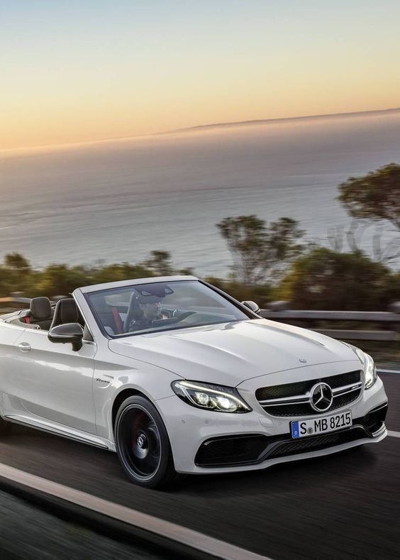 a white mercedes convertible driving on the road near the ocean at sunset or dawn with its roof down