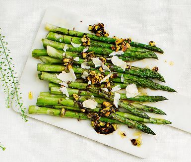 asparagus with parmesan cheese and herbs on a cutting board next to flowers