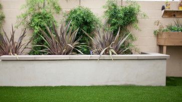 a planter filled with lots of plants on top of a grass covered ground next to a wall