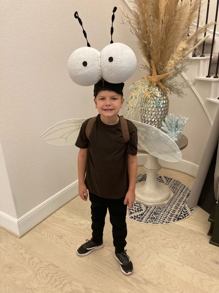 a little boy standing in front of a plant with two bugs on it's head