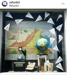 a window display with paper airplanes flying in the air and a globe on top of it