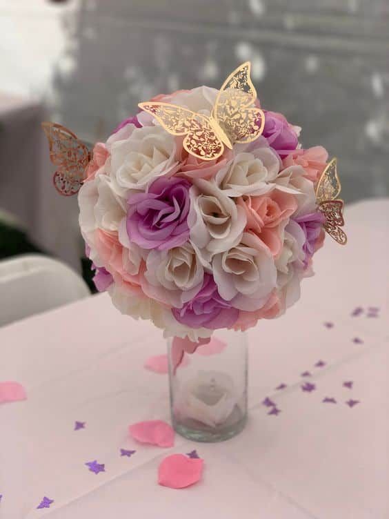 a vase filled with flowers and butterflies on top of a table covered in confetti