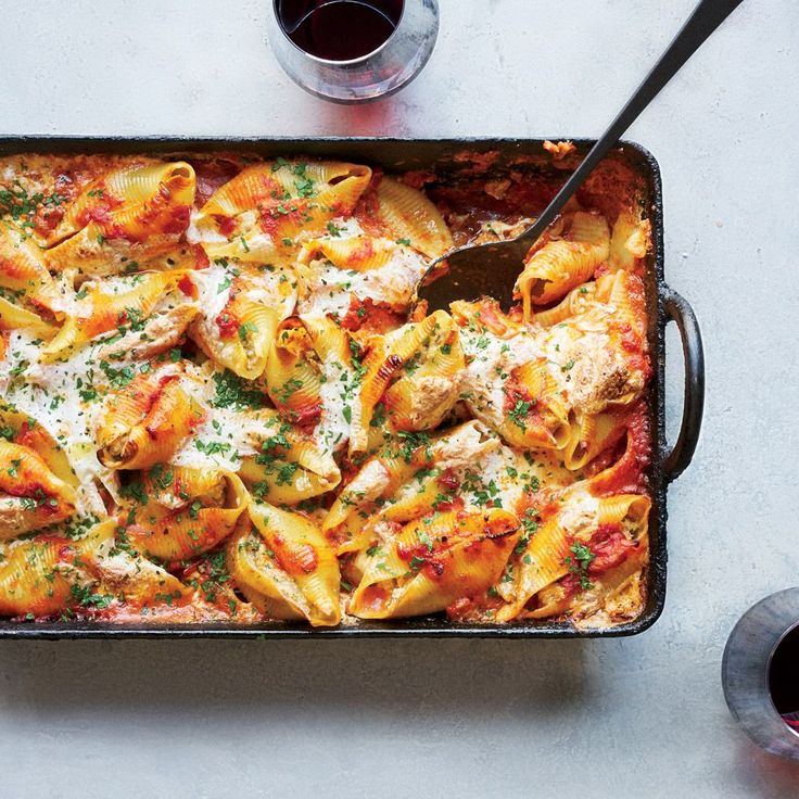 a casserole dish with pasta and meat in it next to a glass of wine