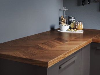 a wooden counter top in a kitchen next to a sink and cabinets with utensils on it