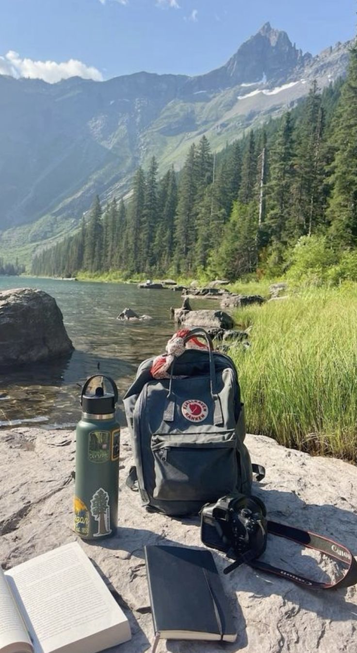 a backpack, book and water bottle sitting on the edge of a cliff overlooking a mountain lake