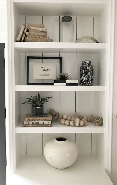 a white shelf with books and vase on top