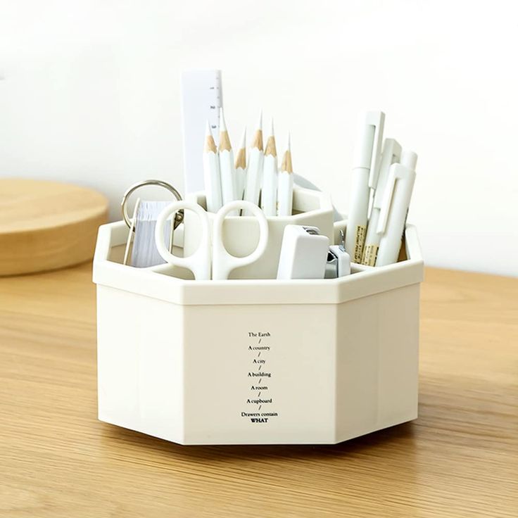 there is a white cup with pens and pencils in it on the table next to a pen holder