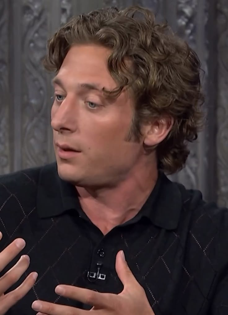 a man with curly hair is holding his hands out and looking to the side while wearing a black shirt