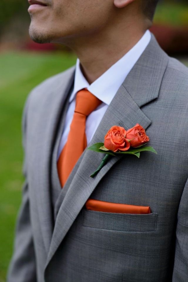 a man in a gray suit with an orange tie and flower boutonniere