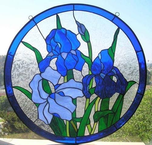 a round stained glass window with blue flowers in the center and greenery behind it