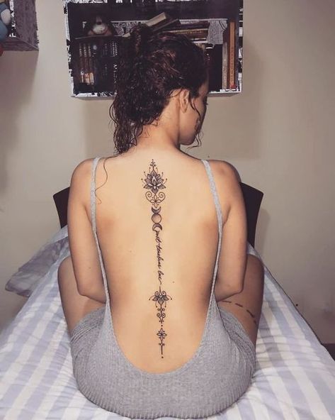 a woman sitting on top of a bed with a tattoo on her back