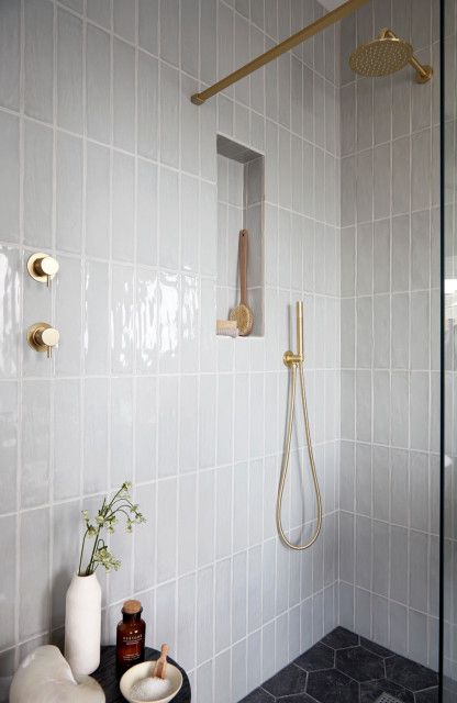 a white tiled bathroom with gold fixtures and black countertop, along with a shower head