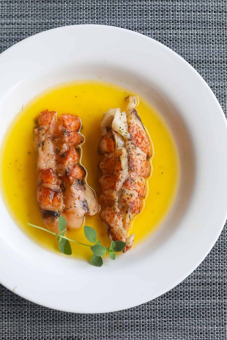 two pieces of meat on a white plate with yellow sauce and green garnish