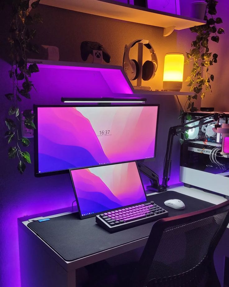 a desk with a laptop, monitor and keyboard on it in front of a purple light