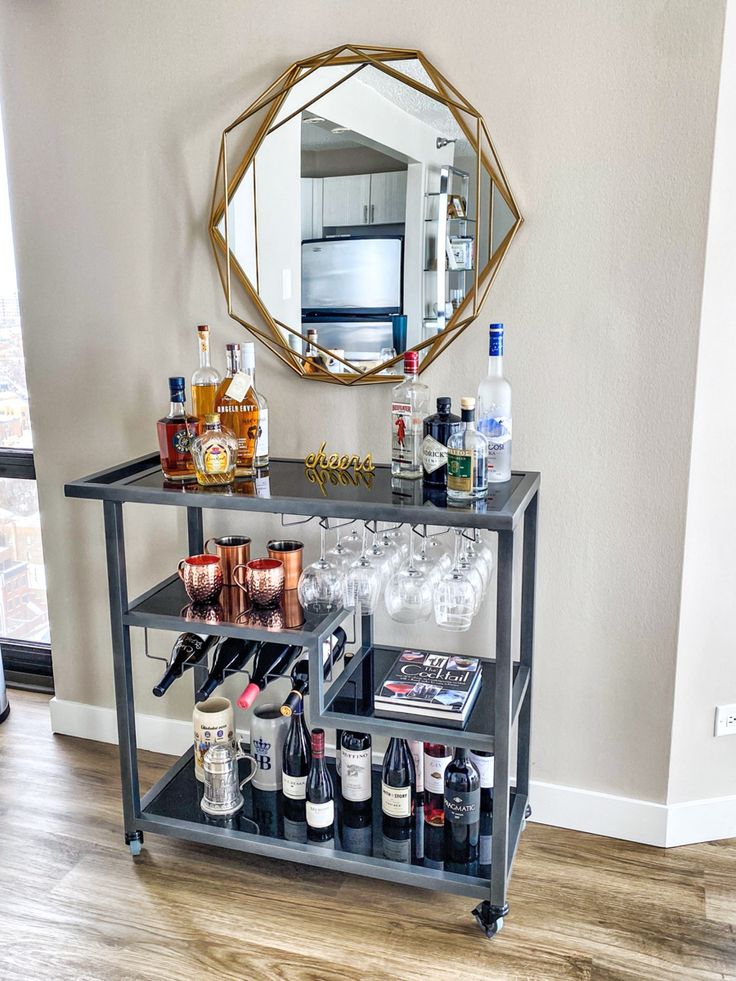 a bar cart with liquor bottles and glasses on it in front of a wall mounted mirror