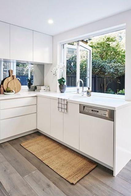 a kitchen with white cabinets and wood flooring next to a large window that looks out onto the backyard