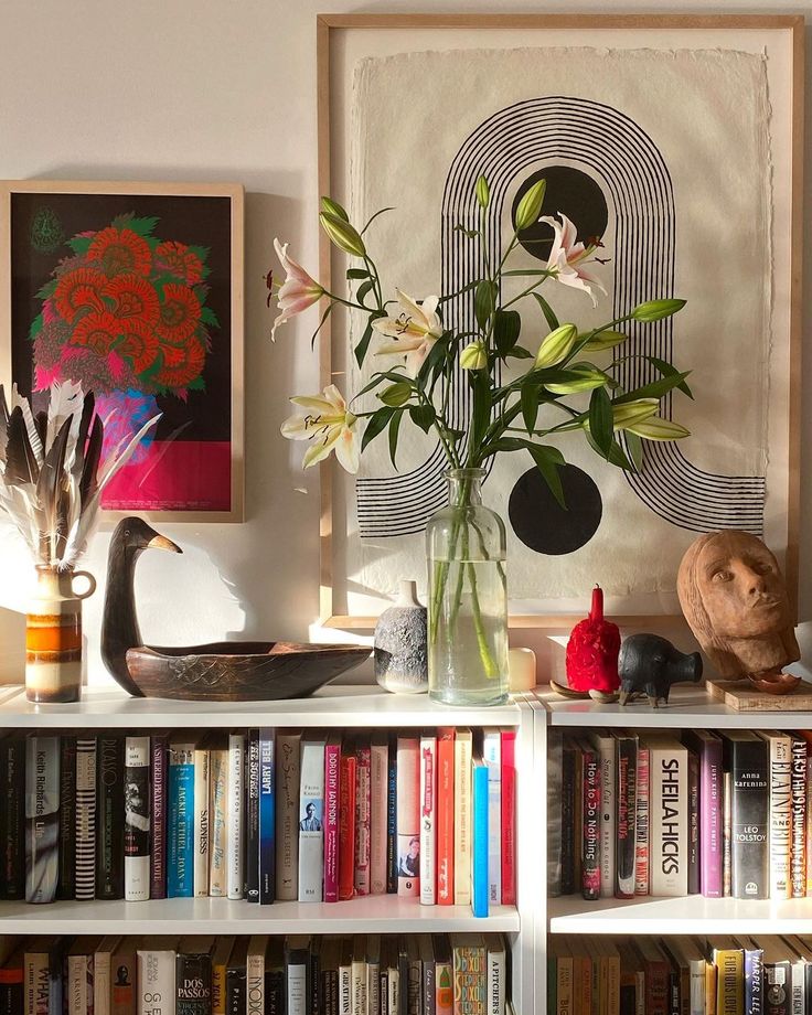 a vase filled with flowers sitting on top of a book shelf next to a bookshelf