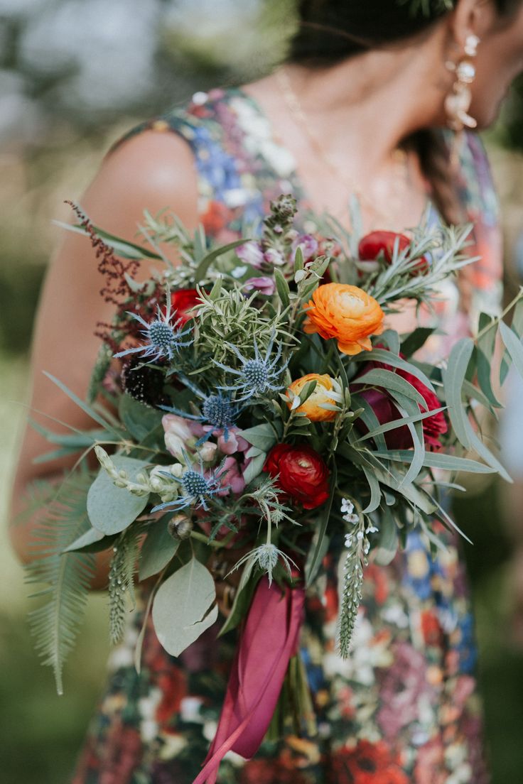 a woman holding a bouquet of flowers and greenery in her hands with an orange rose on it