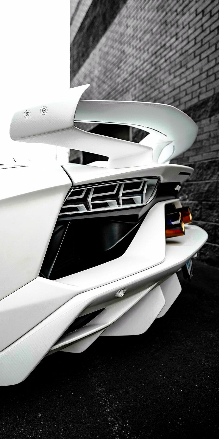 the rear end of a white sports car parked in front of a bricked wall