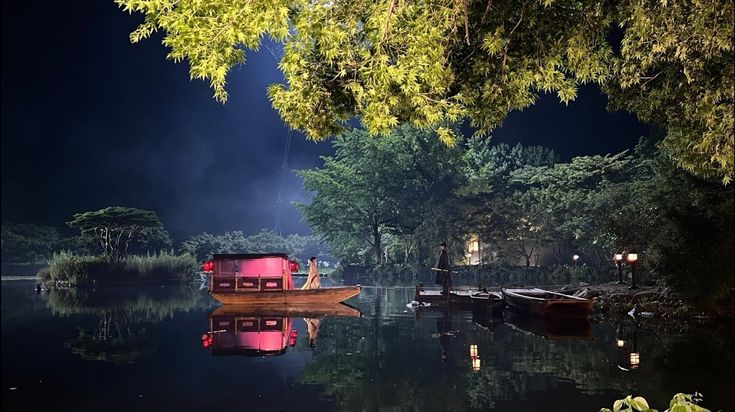 a boat floating on top of a body of water at night with trees in the background