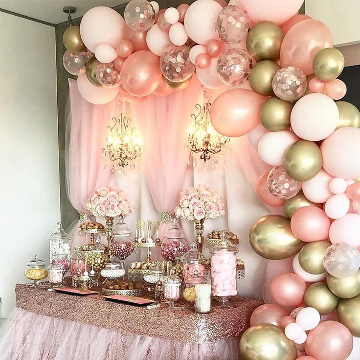 a table topped with lots of pink and gold balloons next to a wall filled with candles