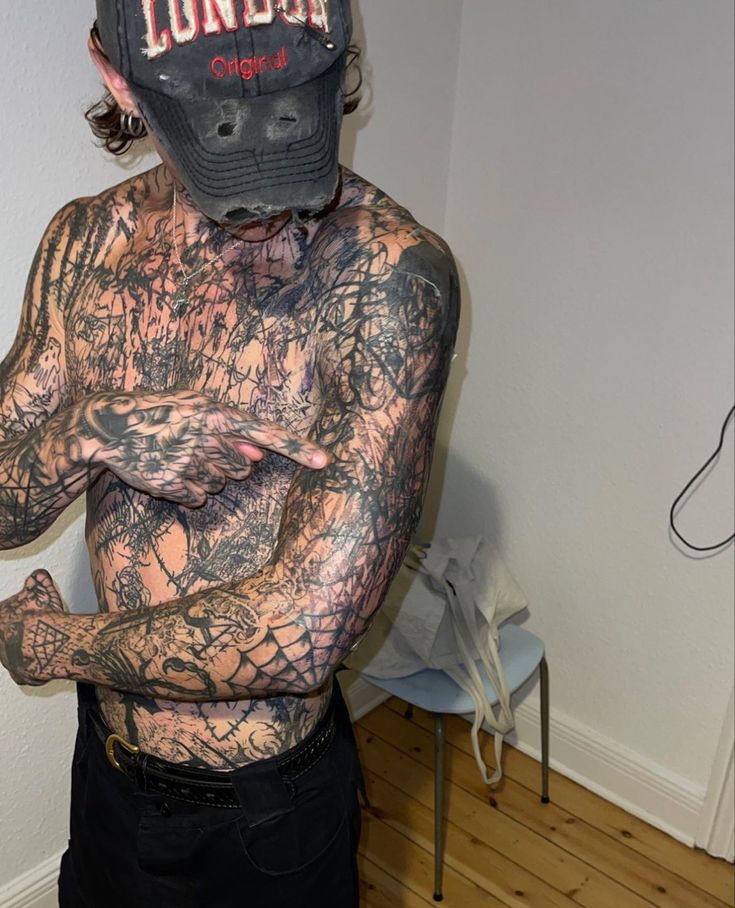 a man with tattoos and a baseball hat on his head is standing in a room