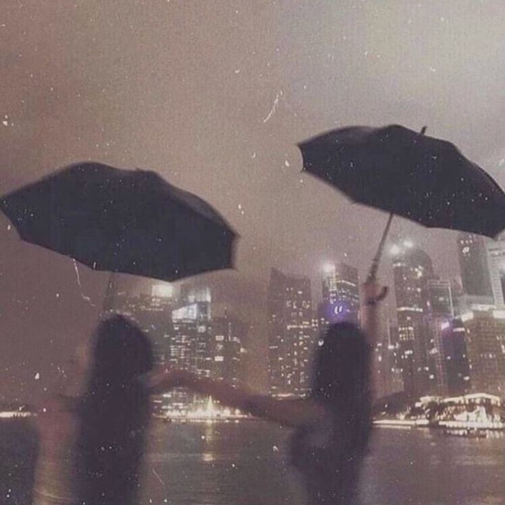 three people holding umbrellas in the rain with their hands up and buildings in the background