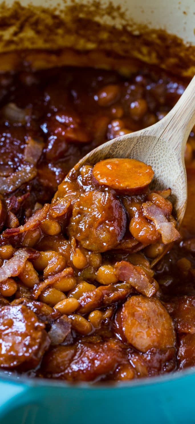 a wooden spoon stirring beans and sausage in a blue pot with brown gravy