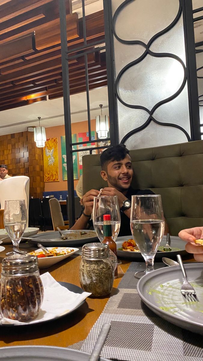 two people sitting at a table with food and drinks in front of them, smiling for the camera