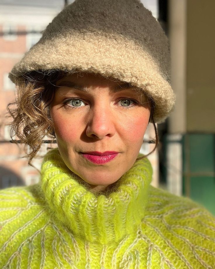 a woman wearing a green sweater with a hat on her head and a scarf around her neck