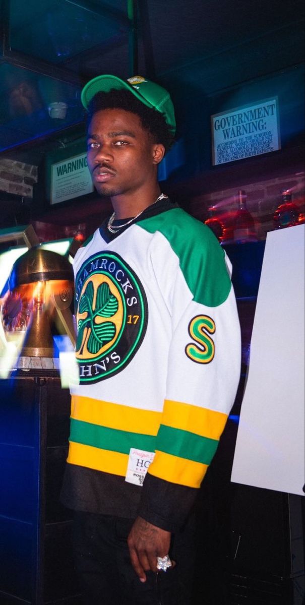 a man standing in front of a bell wearing a green and yellow hockey jersey with the word st patrick's on it