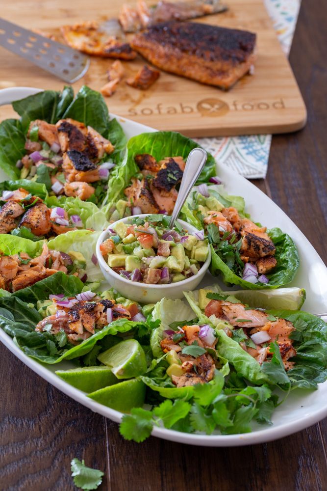 lettuce wraps with salmon and avocado on a white platter next to a cutting board