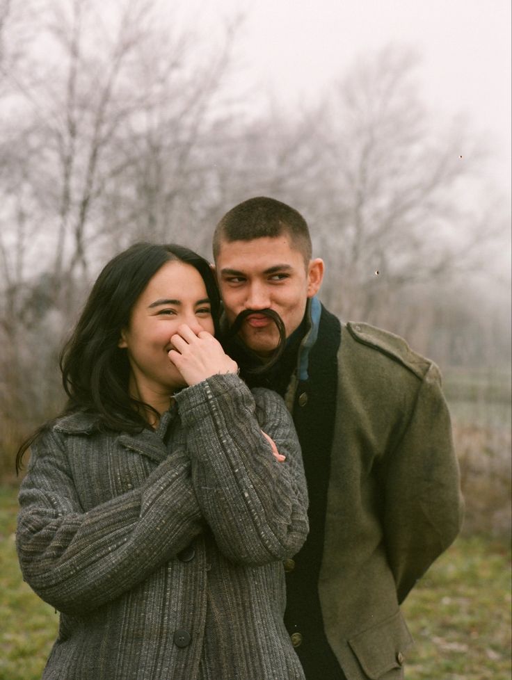 a man and woman standing next to each other in front of some trees with no leaves on them