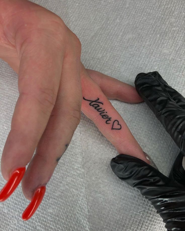 a woman's hand with red fingernails and tattoos on her left thumb, next to a black glove