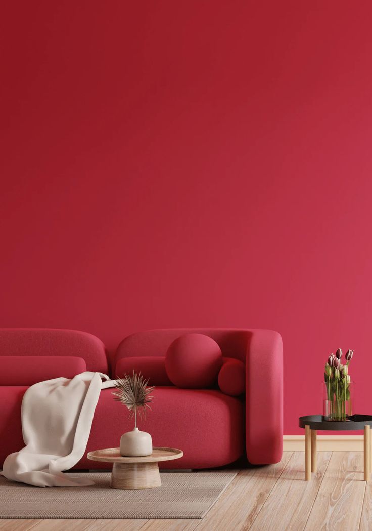 a living room with red walls and wooden flooring, two tables on either side of the couch