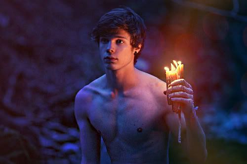 a shirtless young man holding torches in his hand