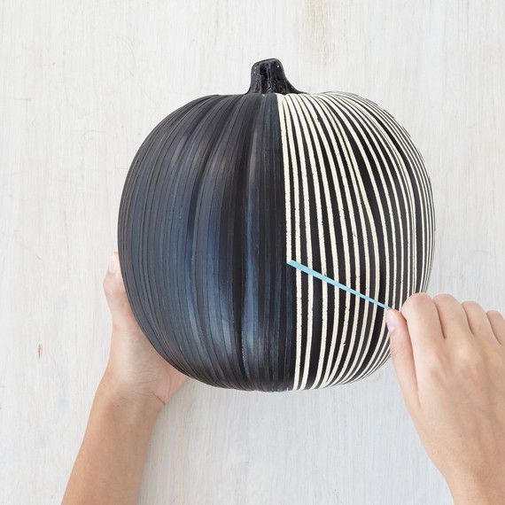 a person holding a black and white striped pumpkin with blue pins sticking out of it