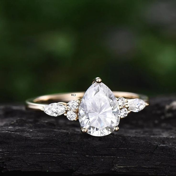 an engagement ring with a pear shaped diamond surrounded by three smaller pears on a piece of wood