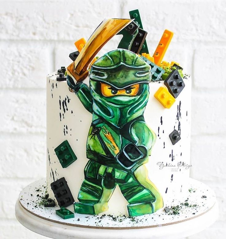 a white cake with green and yellow decorations on it's side, featuring a lego ninja