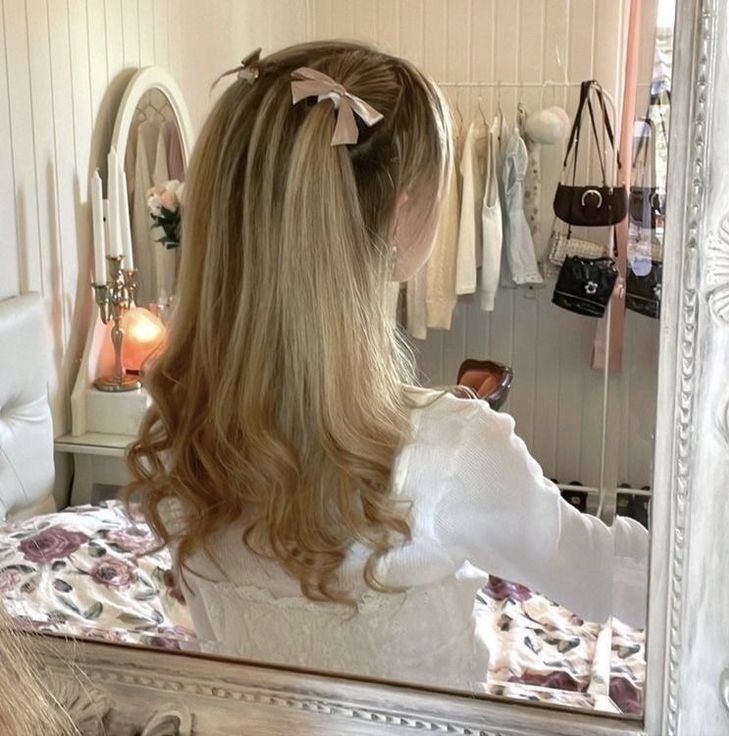 a girl with long blonde hair looking at herself in the mirror while wearing a white dress