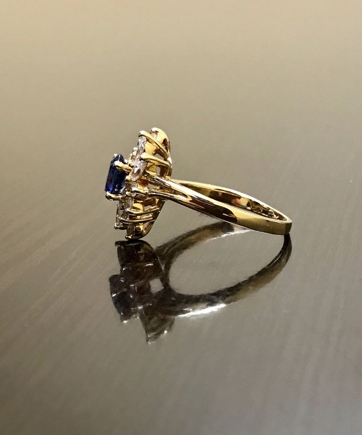 DeKara Designs Clearance Metal- 14K Yellow Gold, .583. Stones- 1 Oval Ceylon Blue Sapphire 0.80 Carats, 4 Marquise Diamonds G Color VS1 Clarity 0.40 Carats, 8 Round Diamonds H Color VS1 Clarity 0.20 Carats. Size- Ring is a 6 3/4, and could be sized up or down at no additional cost! FREE SIZING Handmade 14K Yellow Gold Ceylon Blue Sapphire Halo Diamond Ring. This ring is inspired by the Art Deco era with an enticing fiery oval shaped Ceylon Blue Sapphire. The sapphire is set in between 4 prongs. Formal 14k Gold Sapphire Ring With Halo Design, Blue Marquise Cut Rings For Anniversary, Blue Baguette Cut Rings For Formal Occasions, Formal Blue Baguette Cut Ring, Hallmarked Blue Diamond Wedding Ring, Blue 14k Gold Diamond Ring With Halo Design, Classic Blue Marquise Cut Diamond Ring, Yellow Gold Sapphire Cluster Wedding Ring, Blue 14k Stamped Promise Ring