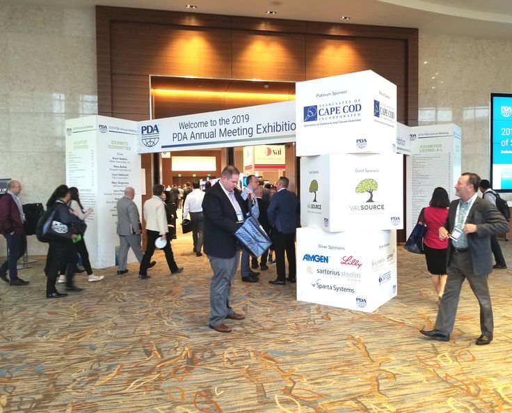 a group of people standing around in front of a large screen at a convention or conference