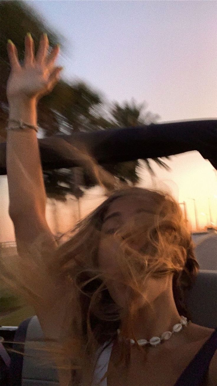 a woman in a car waving her arms up to the sky with palm trees behind her