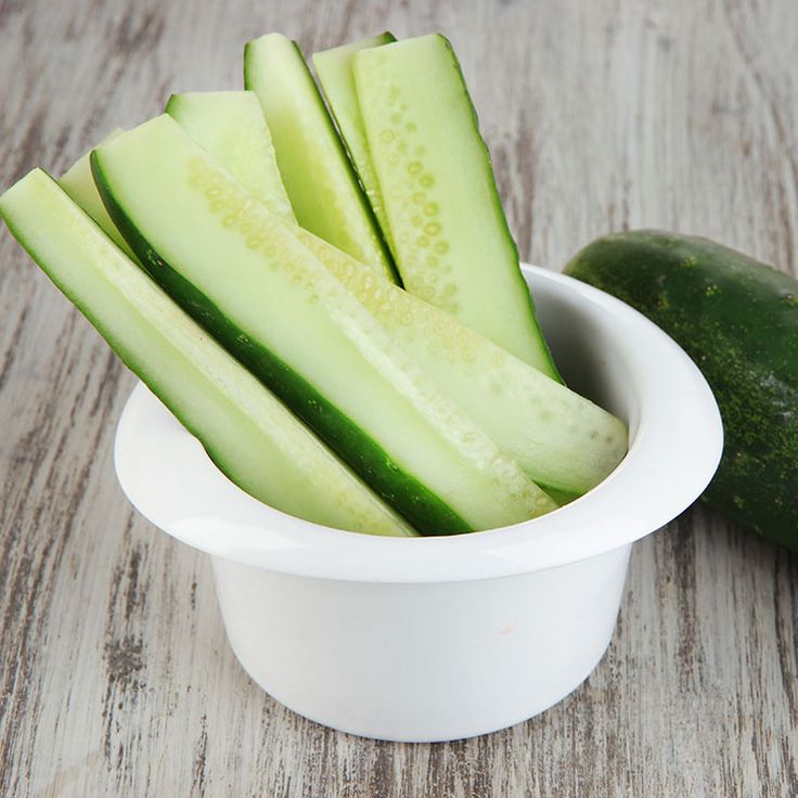 sliced cucumbers in a small white bowl on a wooden table next to a cut up cucumber