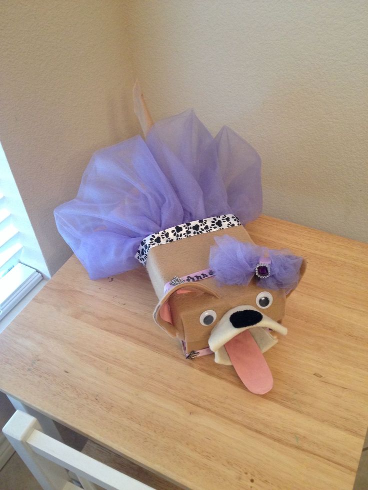 a stuffed dog wearing a purple tutu on top of a wooden table next to a bag