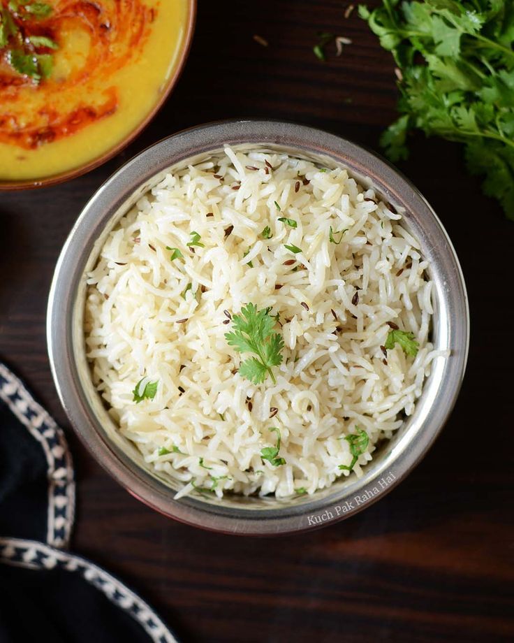 white rice in a metal bowl next to some parsley on a wooden table top